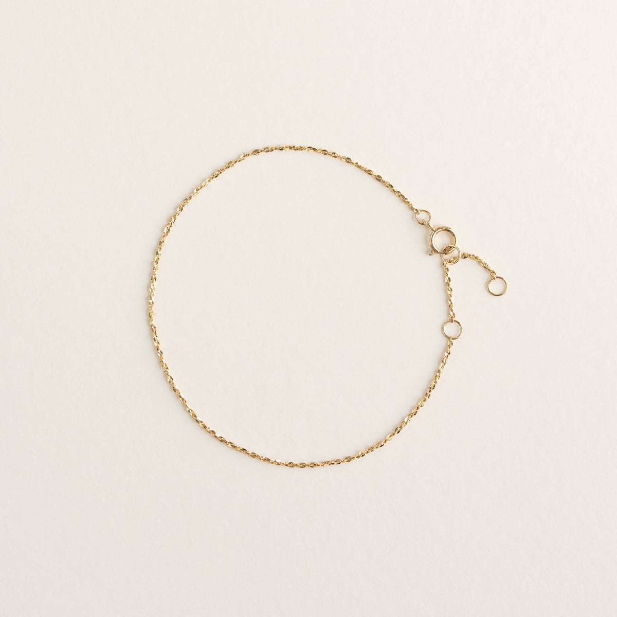 A delicate Gold chain bracelet with a clasp and adjustable links lies flat on a light beige background, conveying elegance and simplicity.