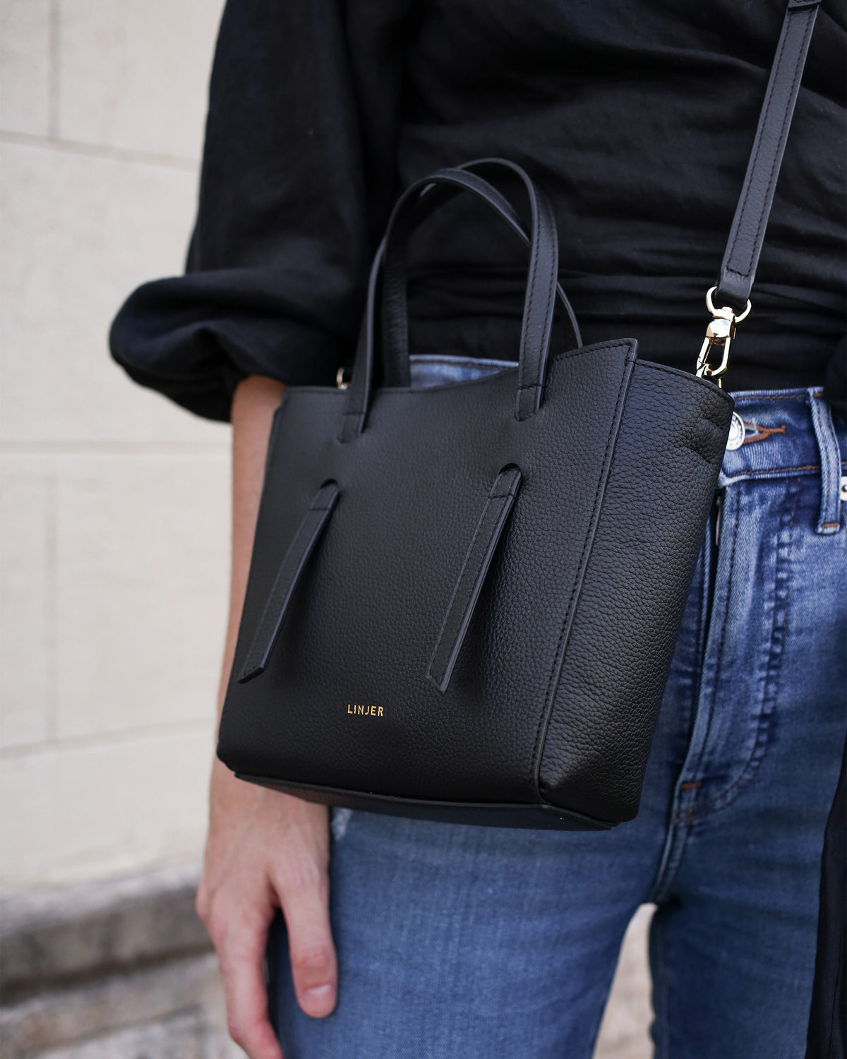 Close-up of a woman wearing The Lana Bag - Maroon with a black top and blue jeans outdoors