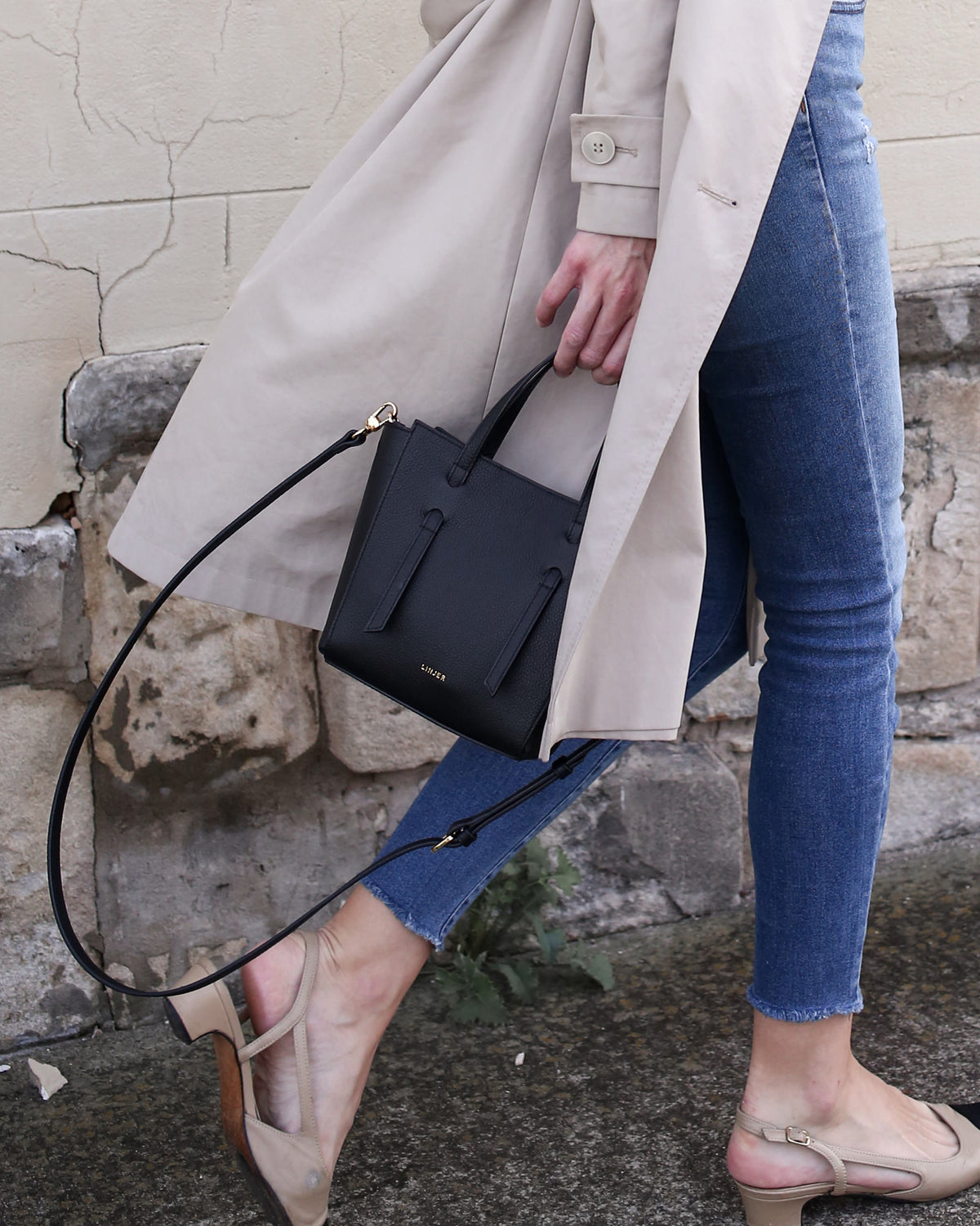 Woman wearing beige trench coat and denim holding The Lana Bag - Maroon mini purse with optional shoulder strap