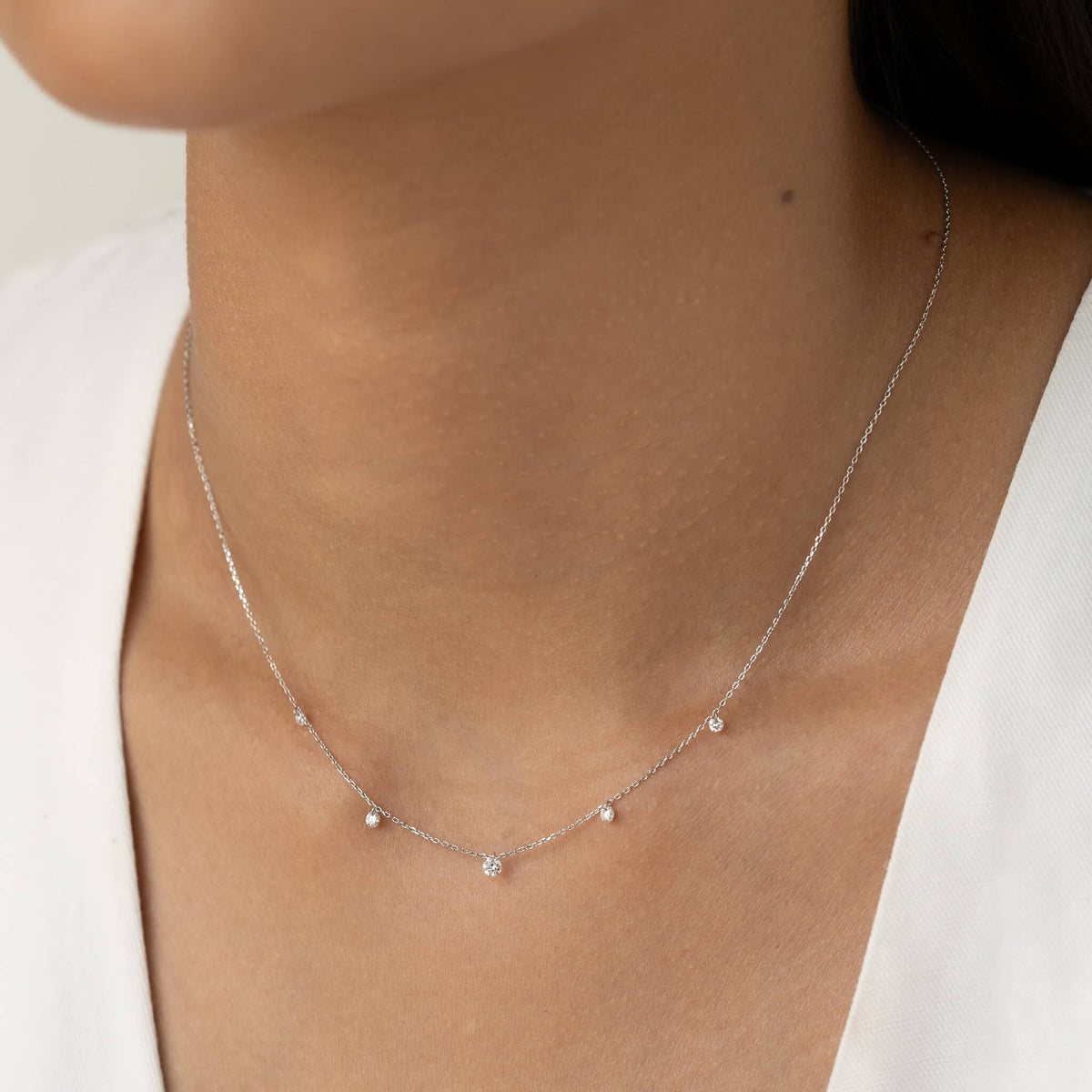 A close-up of a woman's neck wearing a delicate White Gold necklace with evenly spaced small diamonds, set against a light background and white blouse.