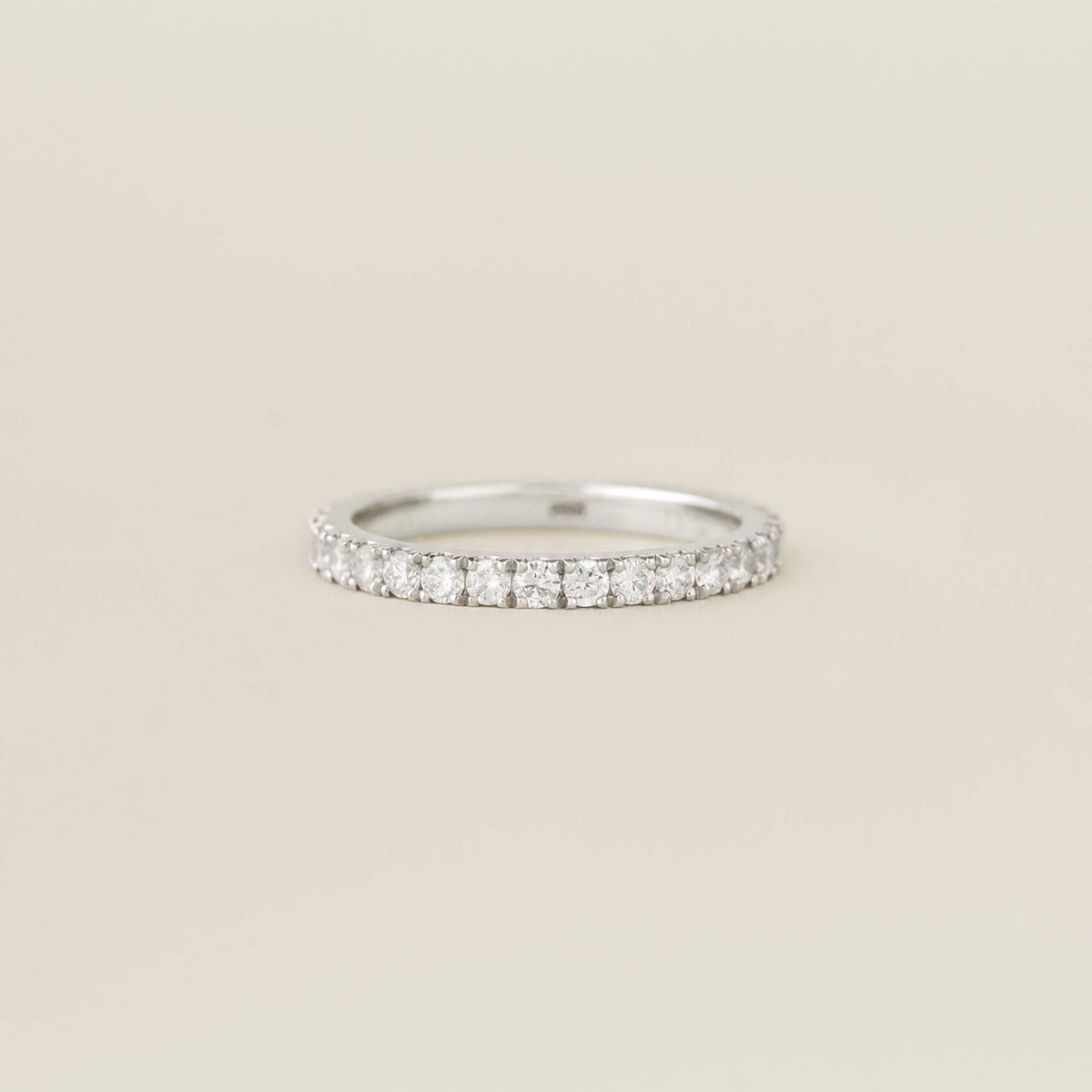 White Gold ring set with a row of small round diamonds on a plain beige background.