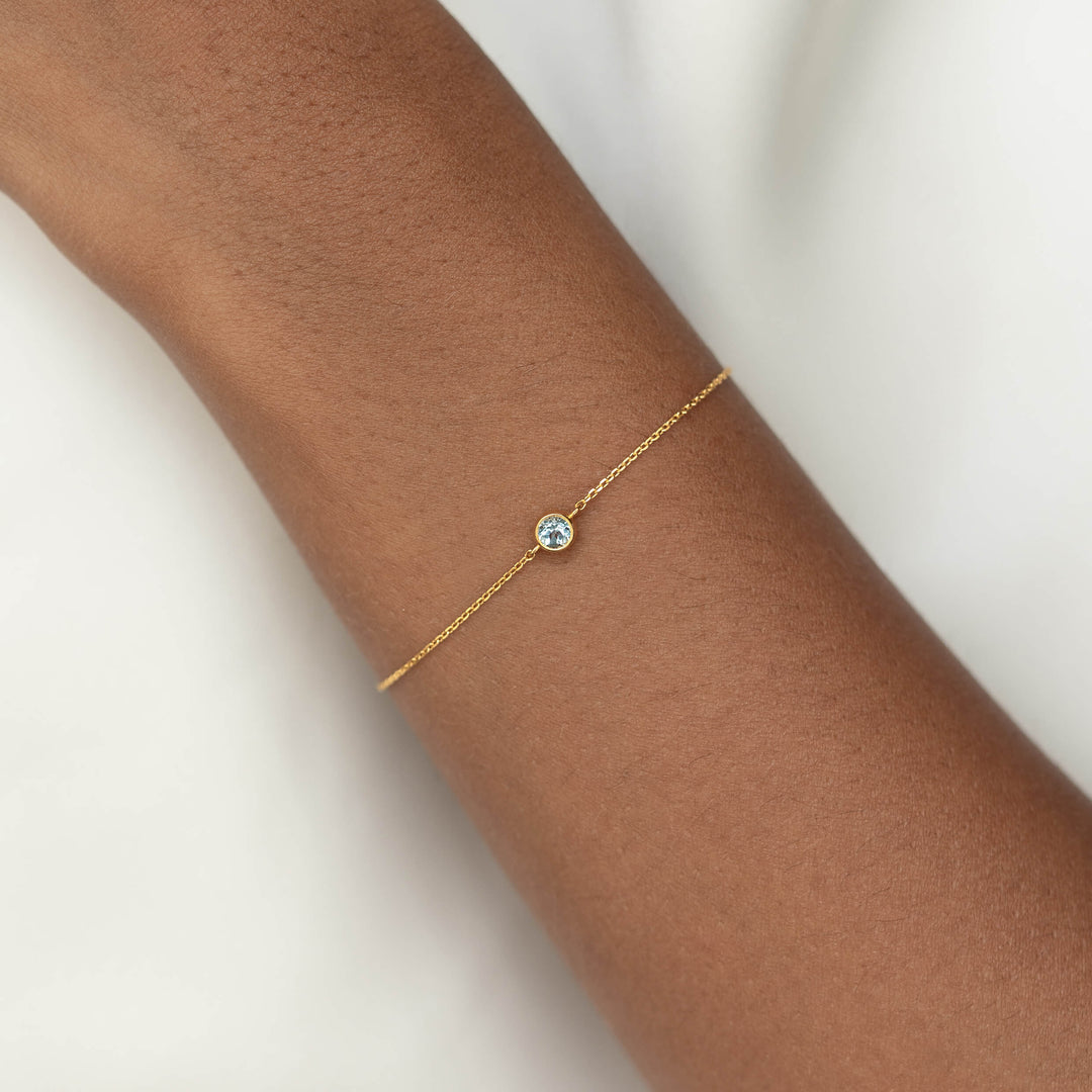 Delicate Gold Vermeil chain bracelet with a small round Blue topaz gemstone centerpiece, worn around a woman's wrist.