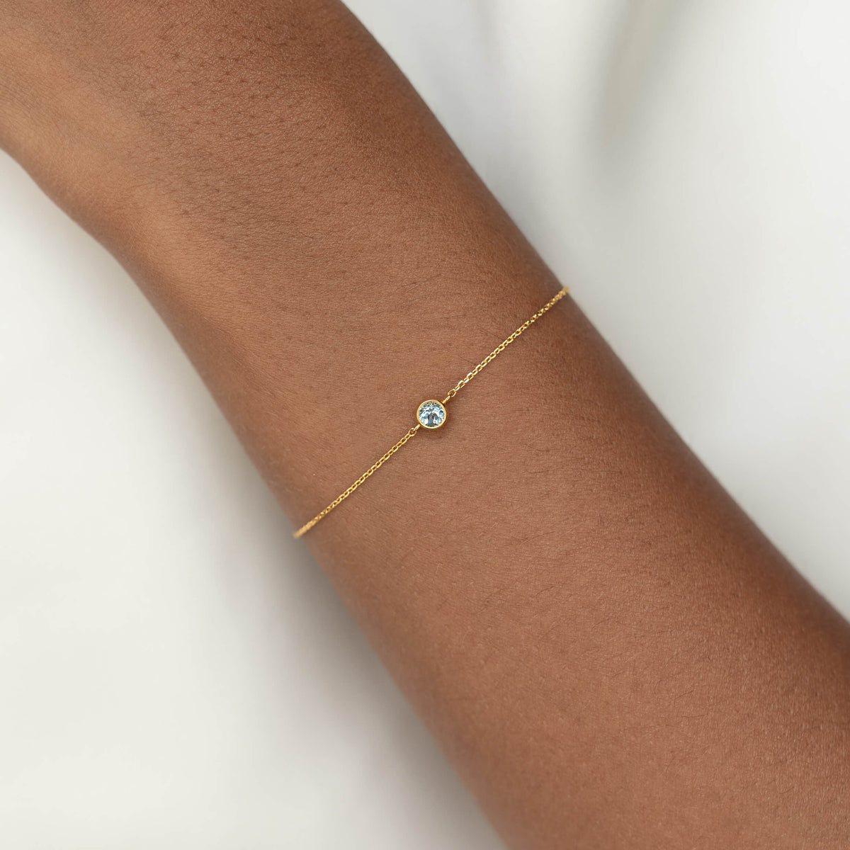 Delicate Gold Vermeil chain bracelet with a small round Blue topaz gemstone centerpiece, worn around a woman's wrist.