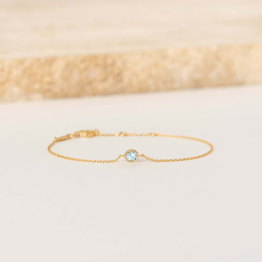 Delicate Gold Vermeil chain bracelet featuring a small round Blue topaz gemstone centerpiece, laid flat on a light-colored surface.