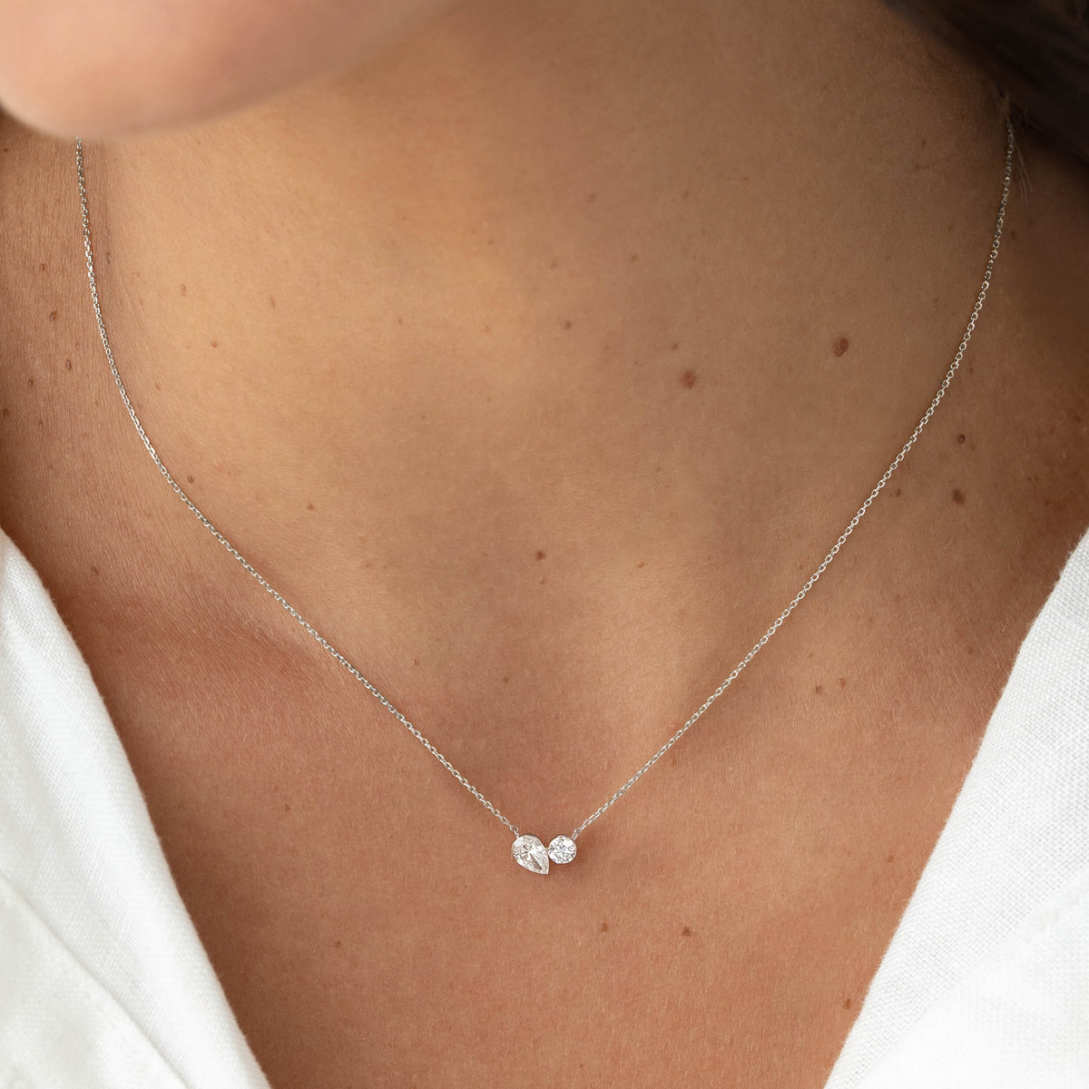 Close-up of a model wearing a delicate White Gold chain necklace with two small diamond accents clustered at the center, resting just above the collarbone against a white top.
