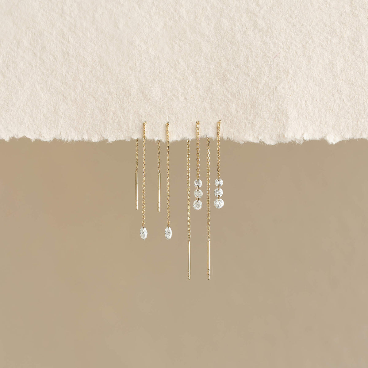 Delicate Gold threader earrings with crystals hang against a soft, beige textured background. The design is elegant and minimalist, conveying sophistication.