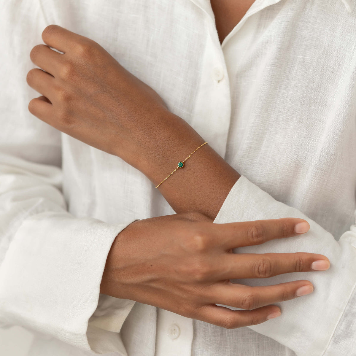 Close-up of a person wearing a white linen blouse, gently resting one hand shoulder while showcasing a delicate Gold Vermeil bracelet with a small Green chalcedony gemstone centerpiece.