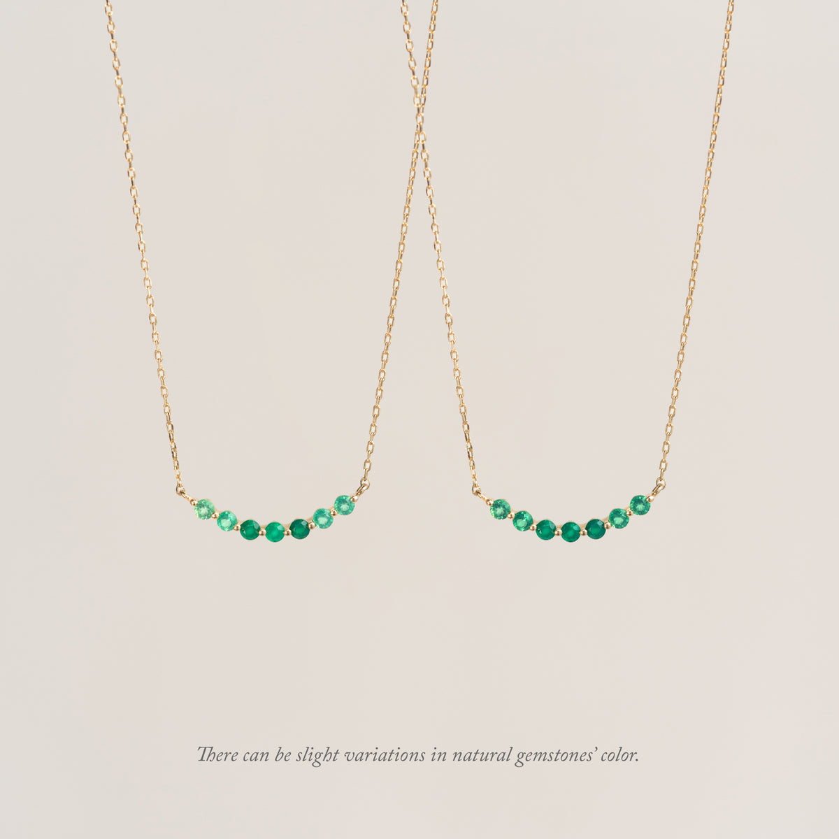 Two delicate gold chain necklaces, each featuring a row of small green gemstones. Text reads, "There can be slight variations in natural gemstones' color."
