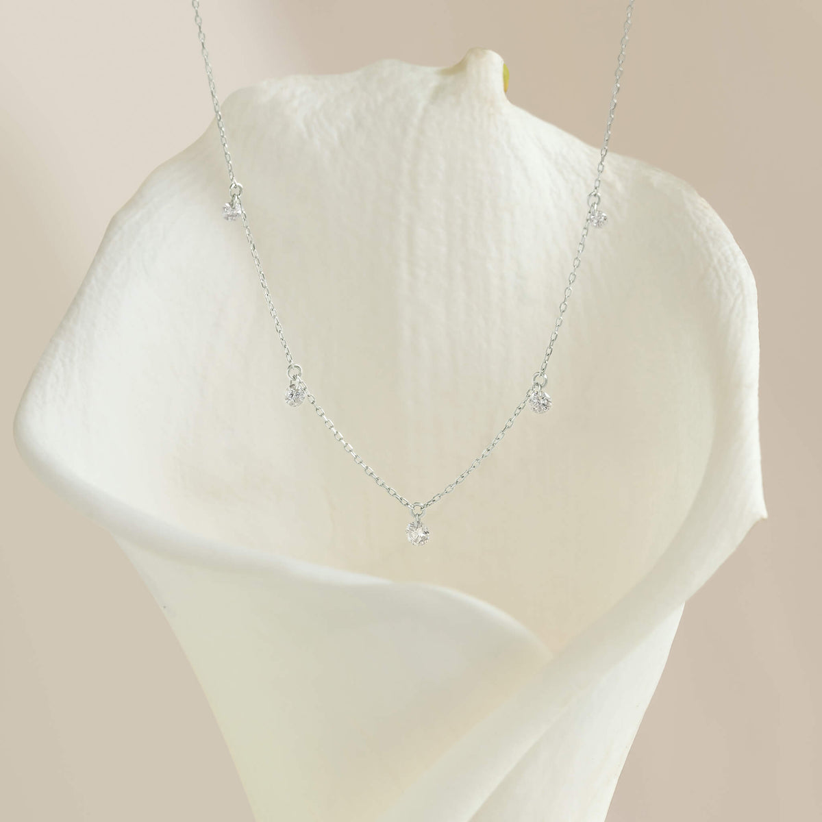 Delicate White Gold necklace with sparkling stones draped over an elegant white calla lily. The soft background creates a serene, luxurious mood.