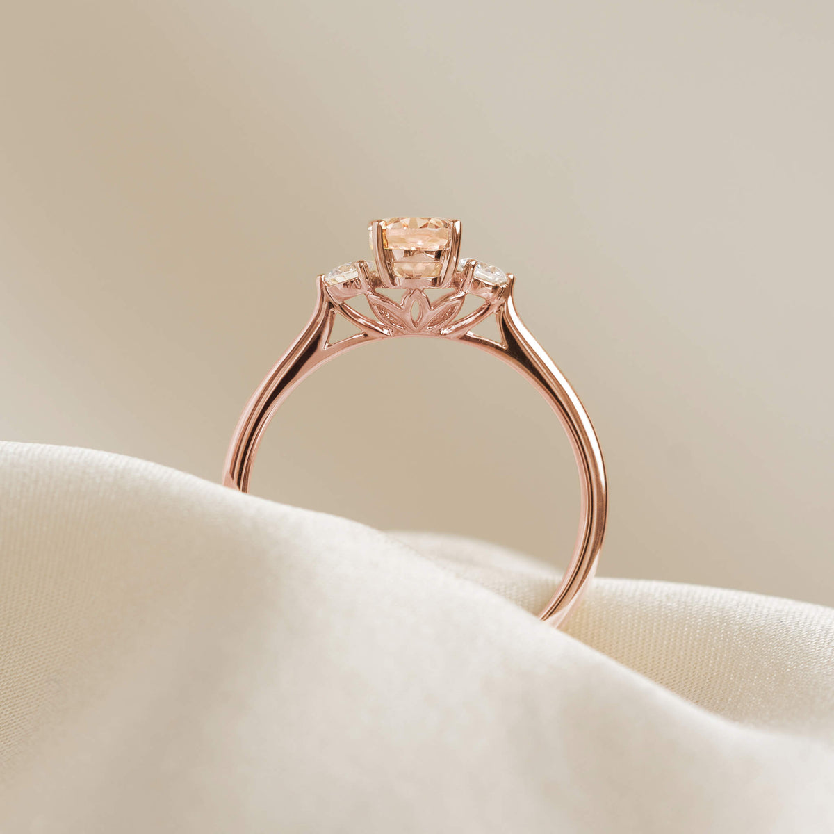 A rose gold ring with a central peach gemstone is elegantly displayed on a soft white fabric, evoking a sense of luxury and refinement.