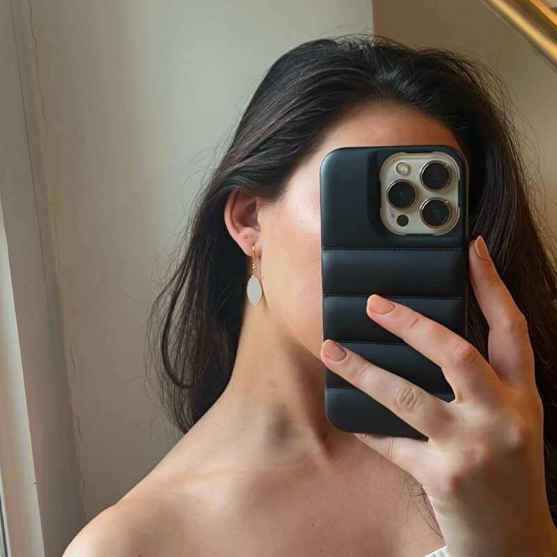 Close-up of a woman with long dark hair wearing a white oval drop earring and holding a phone with black case covering her face