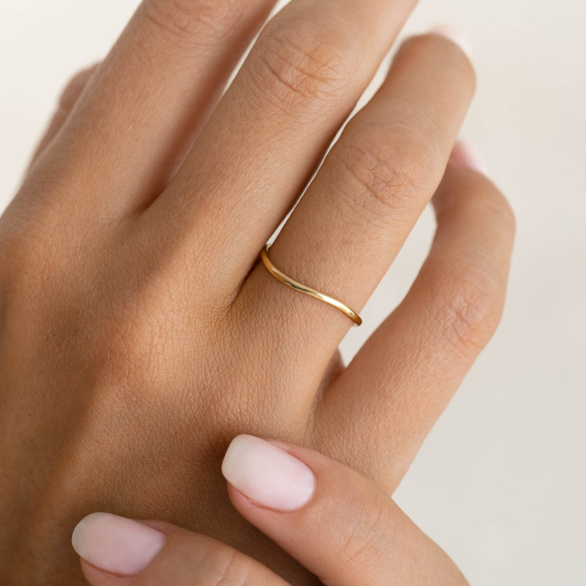 Close-up of a hand wearing the Wavy Ring 14k Gold - Brielle with a natural soft pink manicure on a neutral background