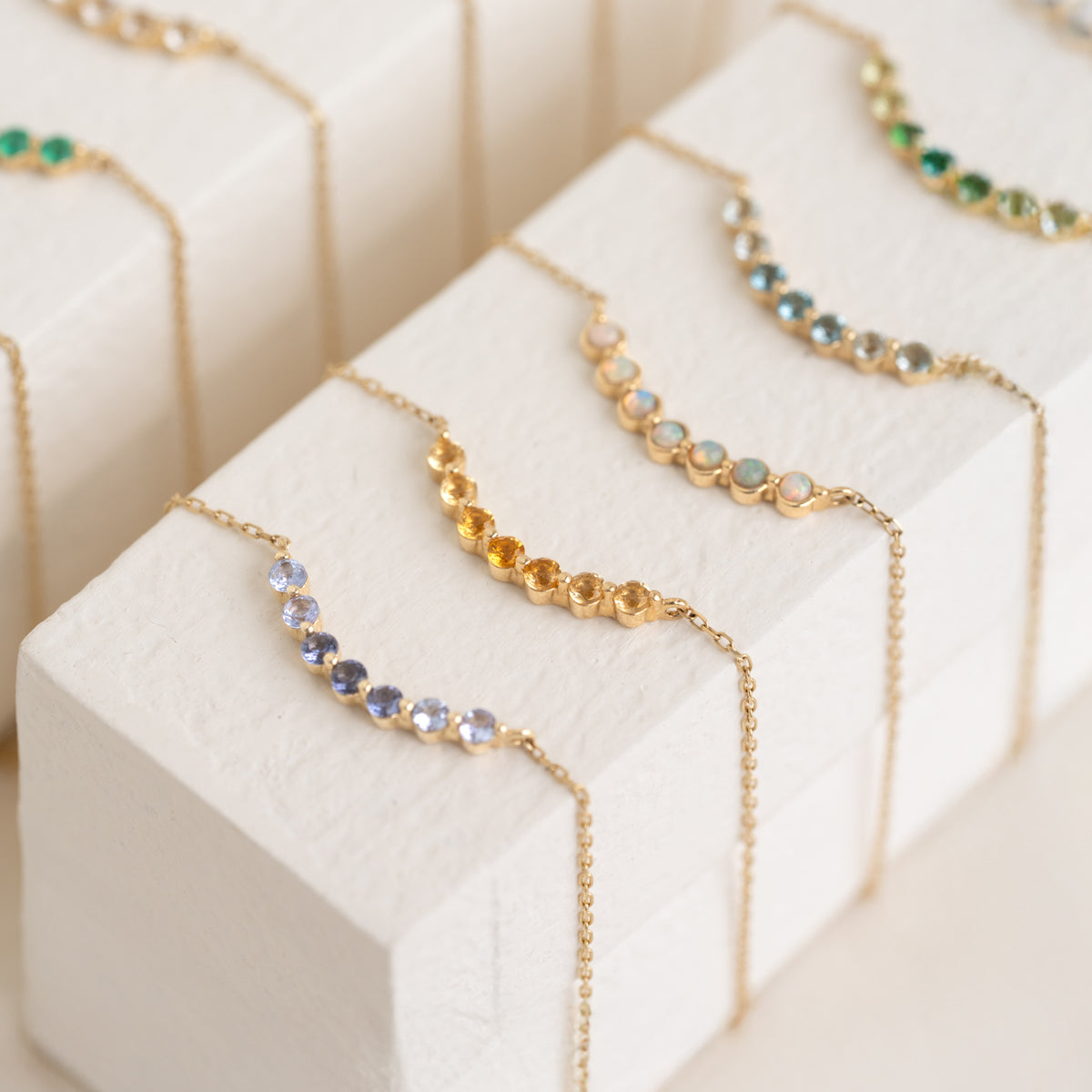 Close-up of October Birthstone Necklace 14k Gold - Opal with opal stones set in a delicate gold chain on a white display block
