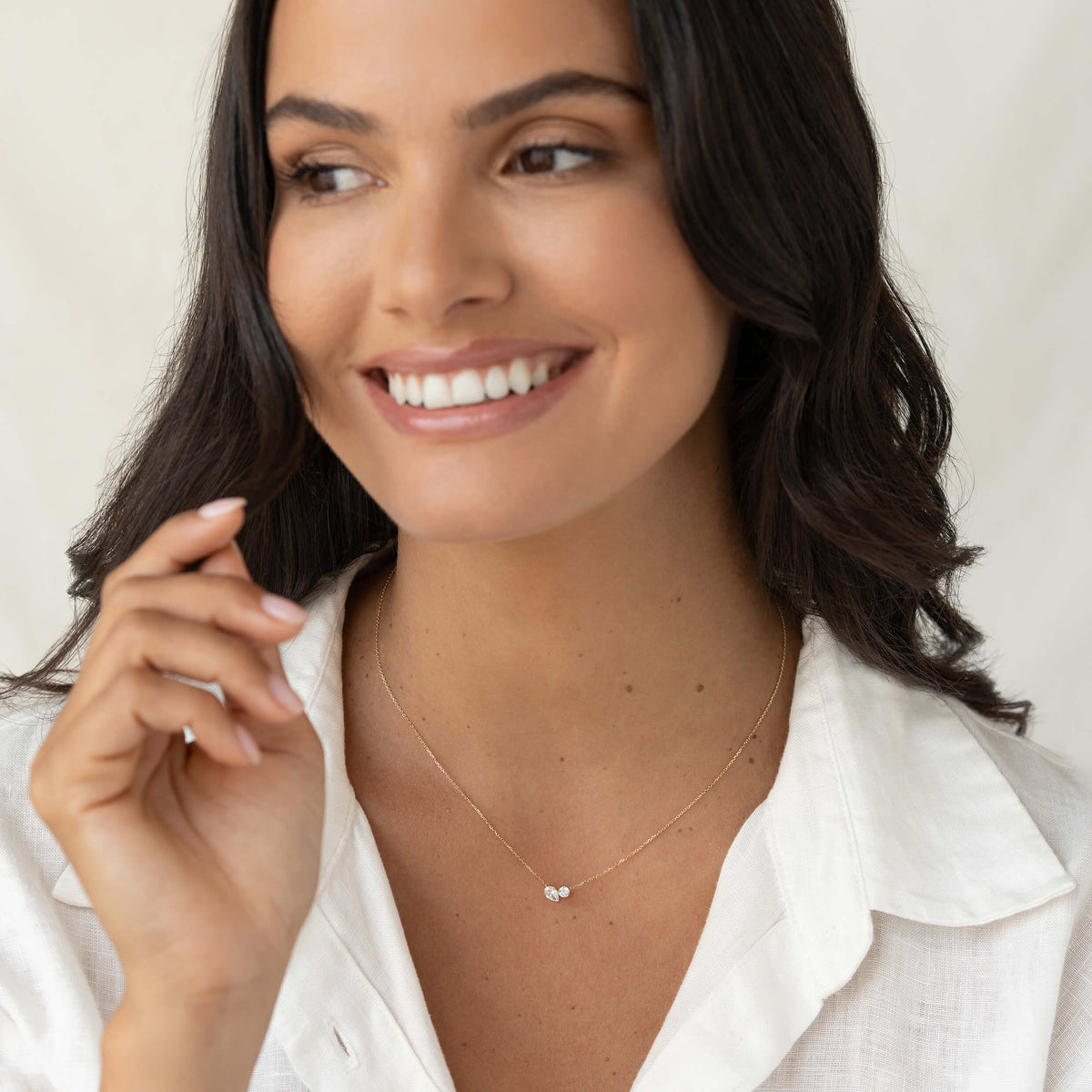 Smiling model wearing a delicate Gold chain necklace with two small diamond pendants paired with a white blouse, shown in a softly lit close-up portrait.
