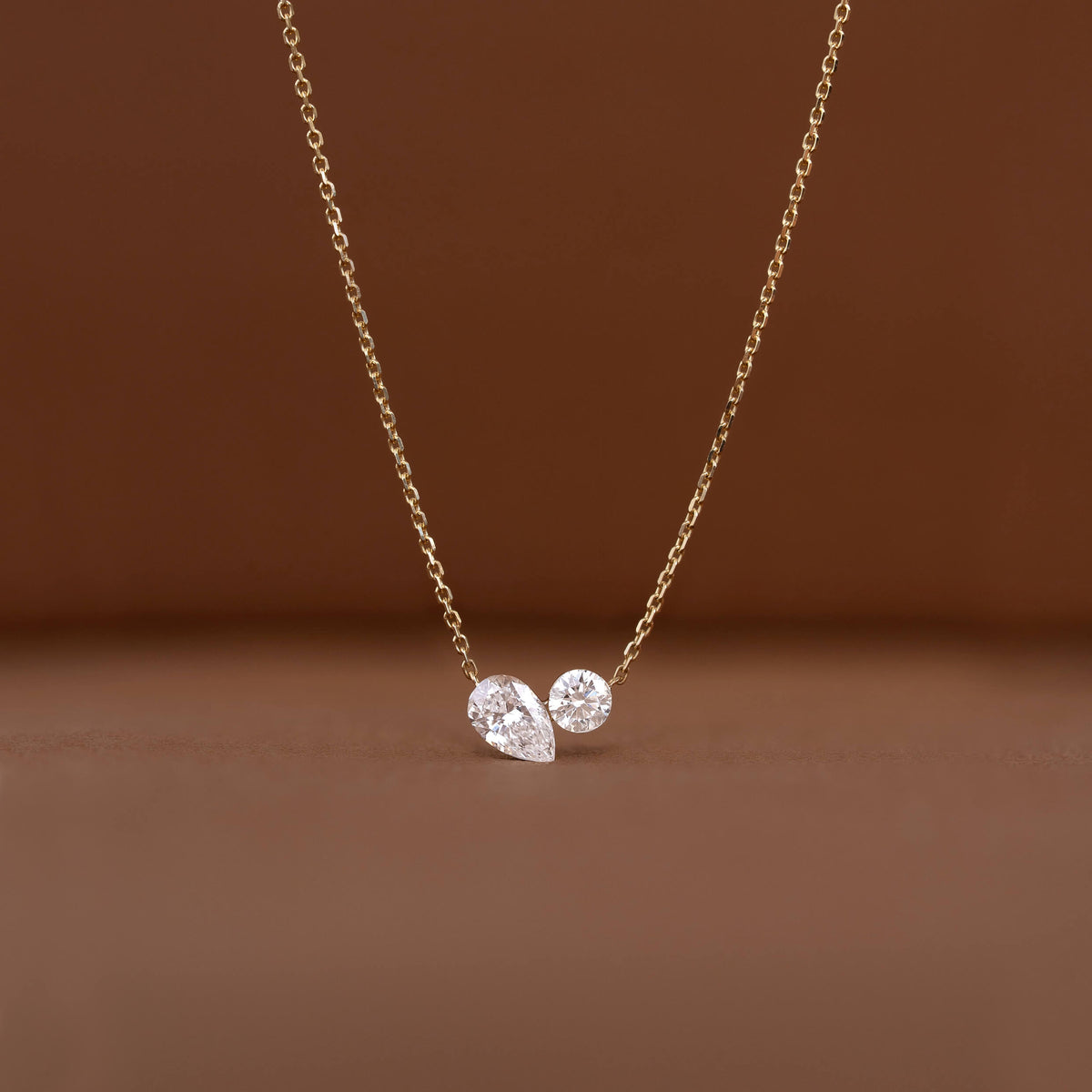 Delicate Gold chain necklace displayed against a warm brown background, featuring two diamond pendants.
