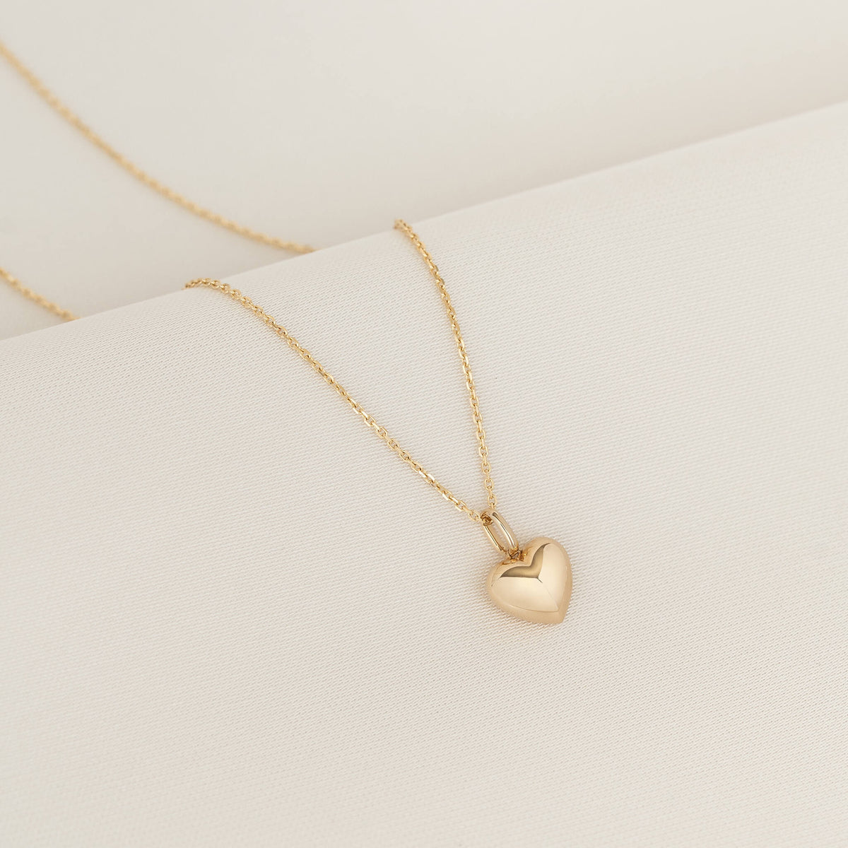 Yellow Gold necklace featuring a faceted heart-shaped pendant displayed on a white textured surface.