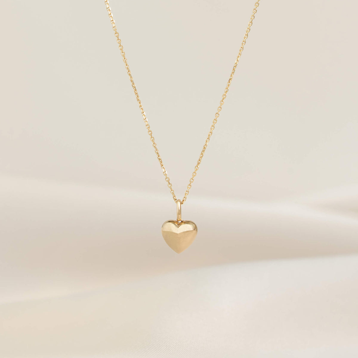 Yellow Gold necklace with a polished heart-shaped pendant, displayed on a delicate chain against a soft neutral background.