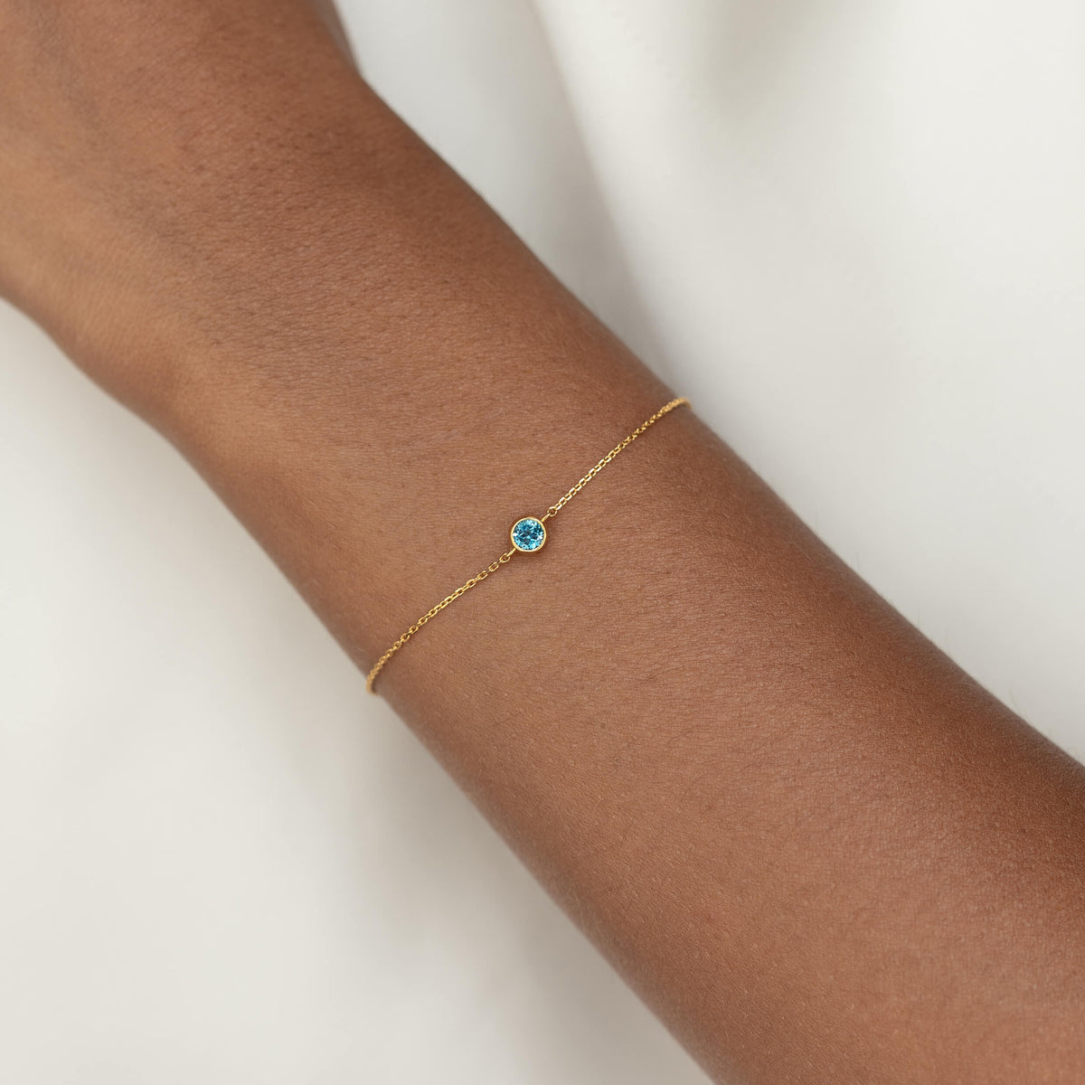 Delicate Gold Vermeil chain bracelet with a small round London blue topaz gemstone centerpiece, worn around a woman's wrist.