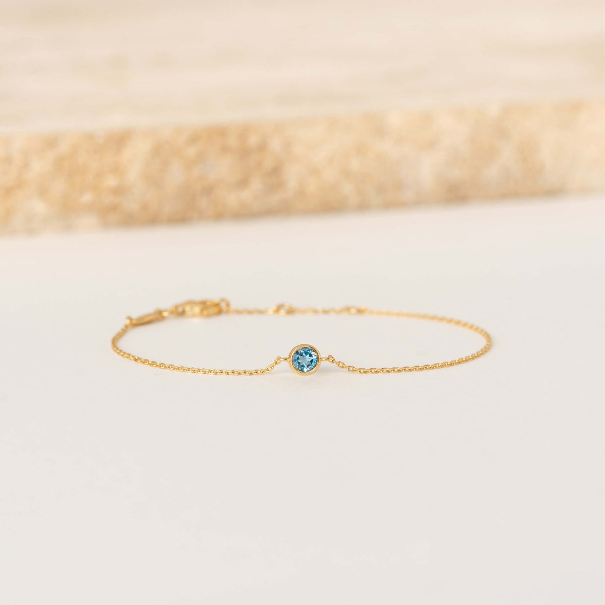 Delicate Gold Vermeil chain bracelet featuring a small round London blue topaz gemstone centerpiece, laid flat on a light-colored surface.