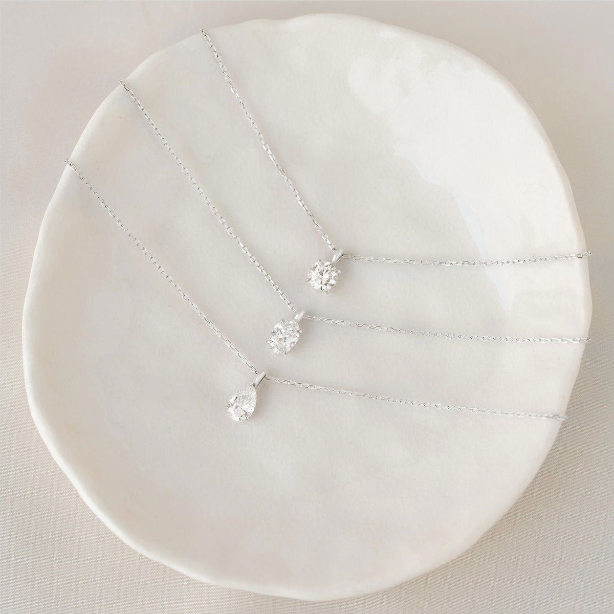 Three silver necklaces with pendant drops on a white circular stand.