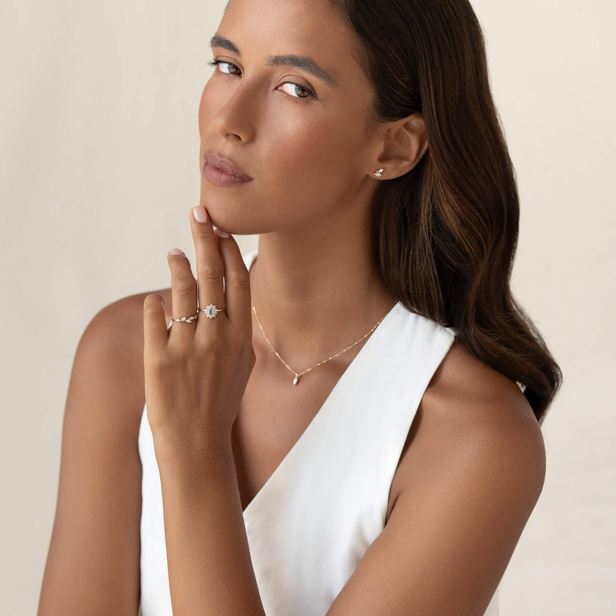 Woman in white dress wearing elegant jewelry: a diamond ring, pearl necklace, and stud earrings. Her expression is thoughtful and serene.
