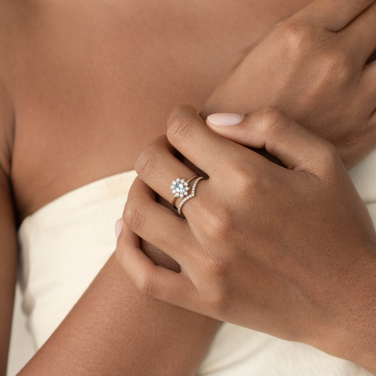 A close-up of a person’s hands showcasing a delicate gold ring with a floral gemstone design. The hands rest gracefully against the chest, conveying elegance.