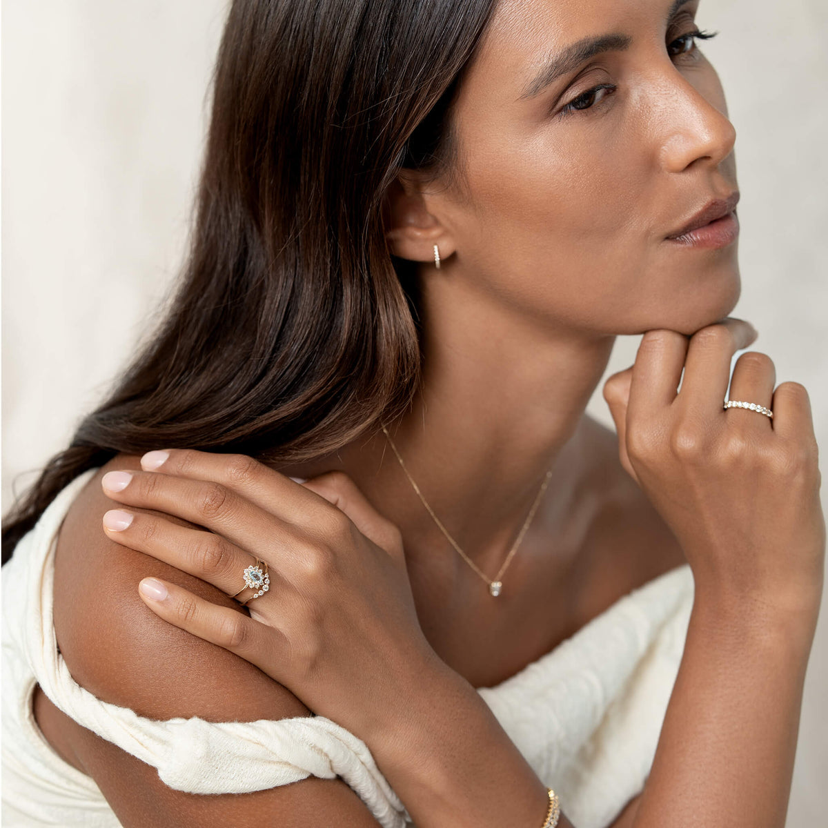A woman poses thoughtfully, showcasing elegant jewelry; a sparkling diamond ring on each hand and a delicate necklace, exuding sophistication and grace.