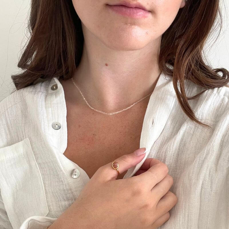 Close-up of a woman wearing a delicate gold ring and a thin necklace with a white button-up shirt background