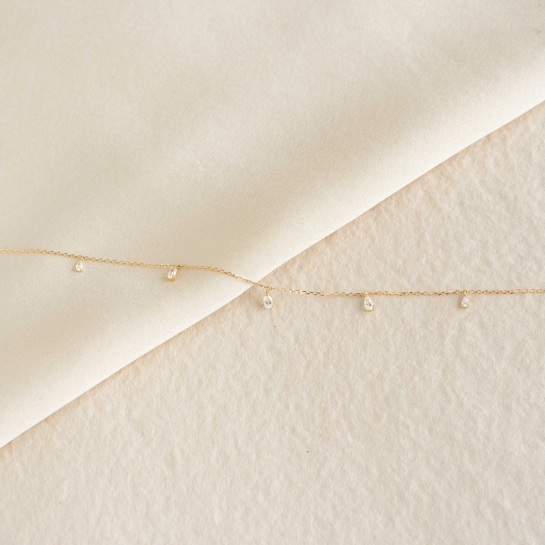 Close-up of Pear Cut Diamond Pendant Necklace 14k Gold - Sylvie with small diamonds on delicate gold chain on cream background