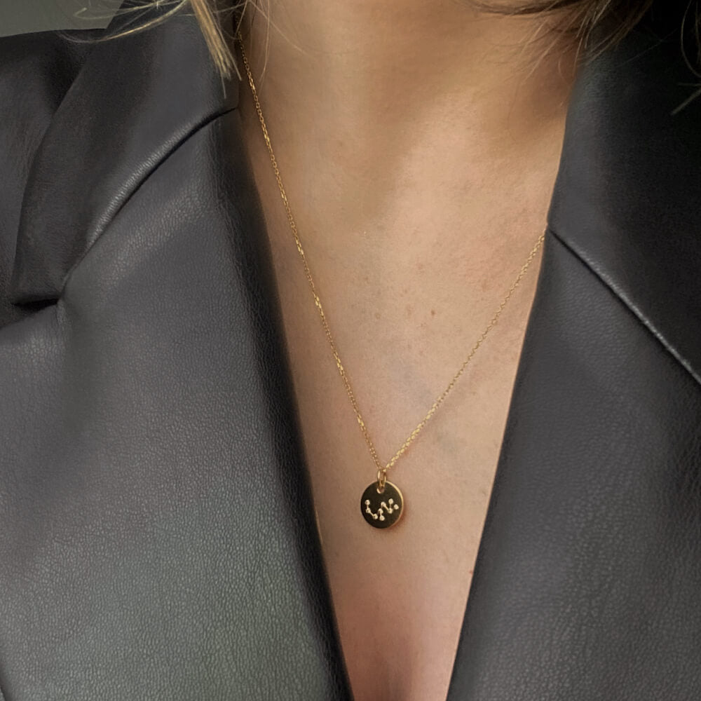 Close-up of a gold pendant necklace with constellation design worn over a black leather jacket collar